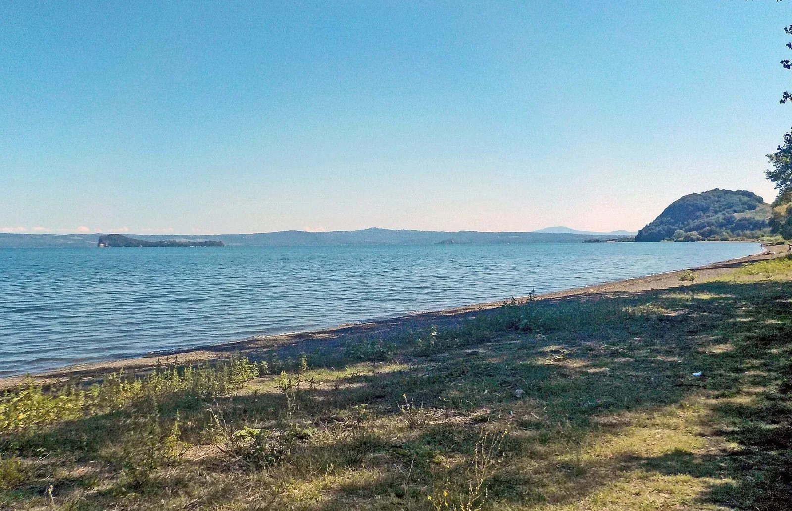 Le isole Bisentina e Martana nel lago di Bolsena viste da una riva erbosa, con le colline sullo sfondo